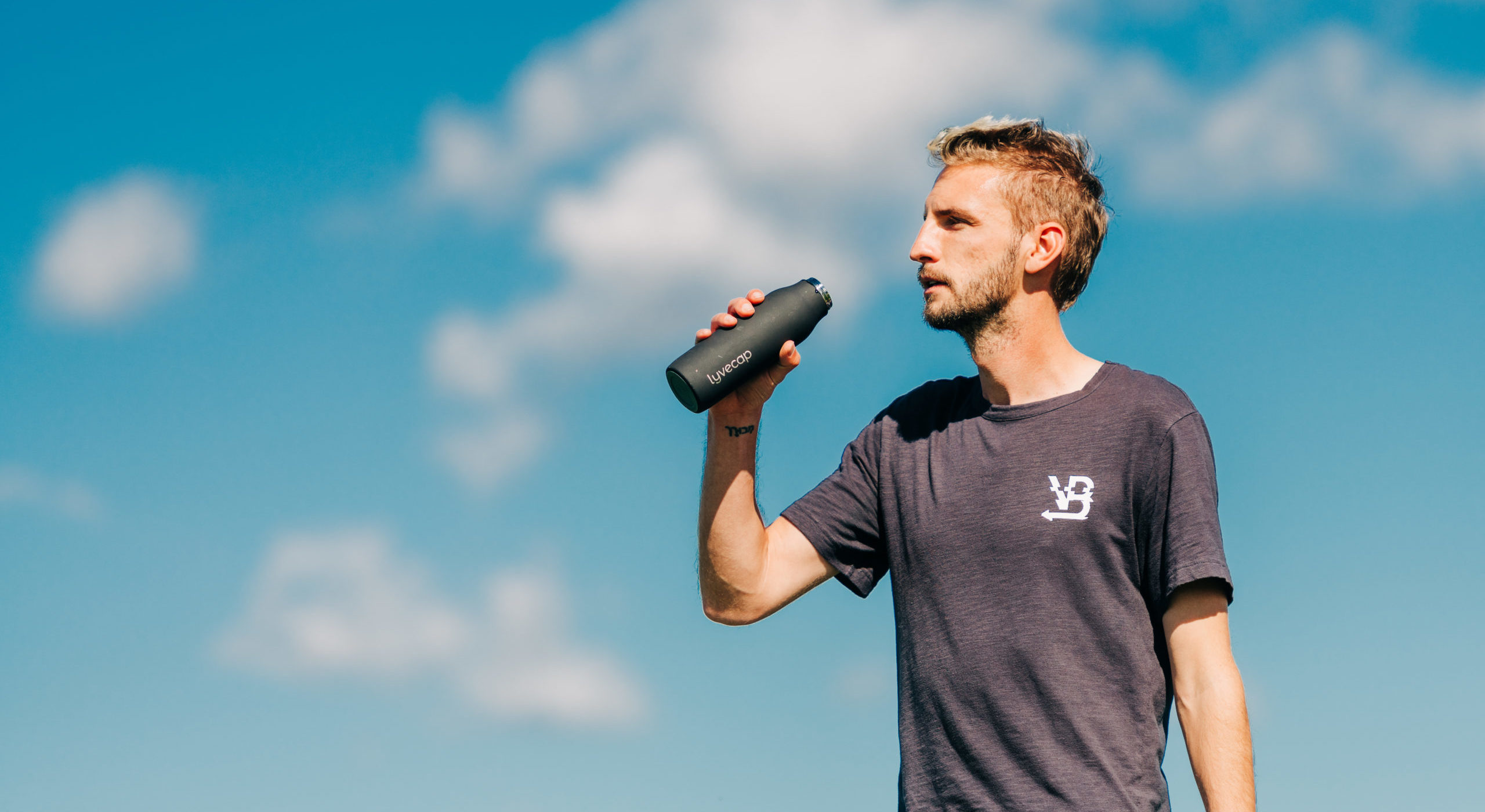 color image of pro soccer player Villyan Bijev holding a LYVECAP probiotic water bottle against a blue sky with white clouds
