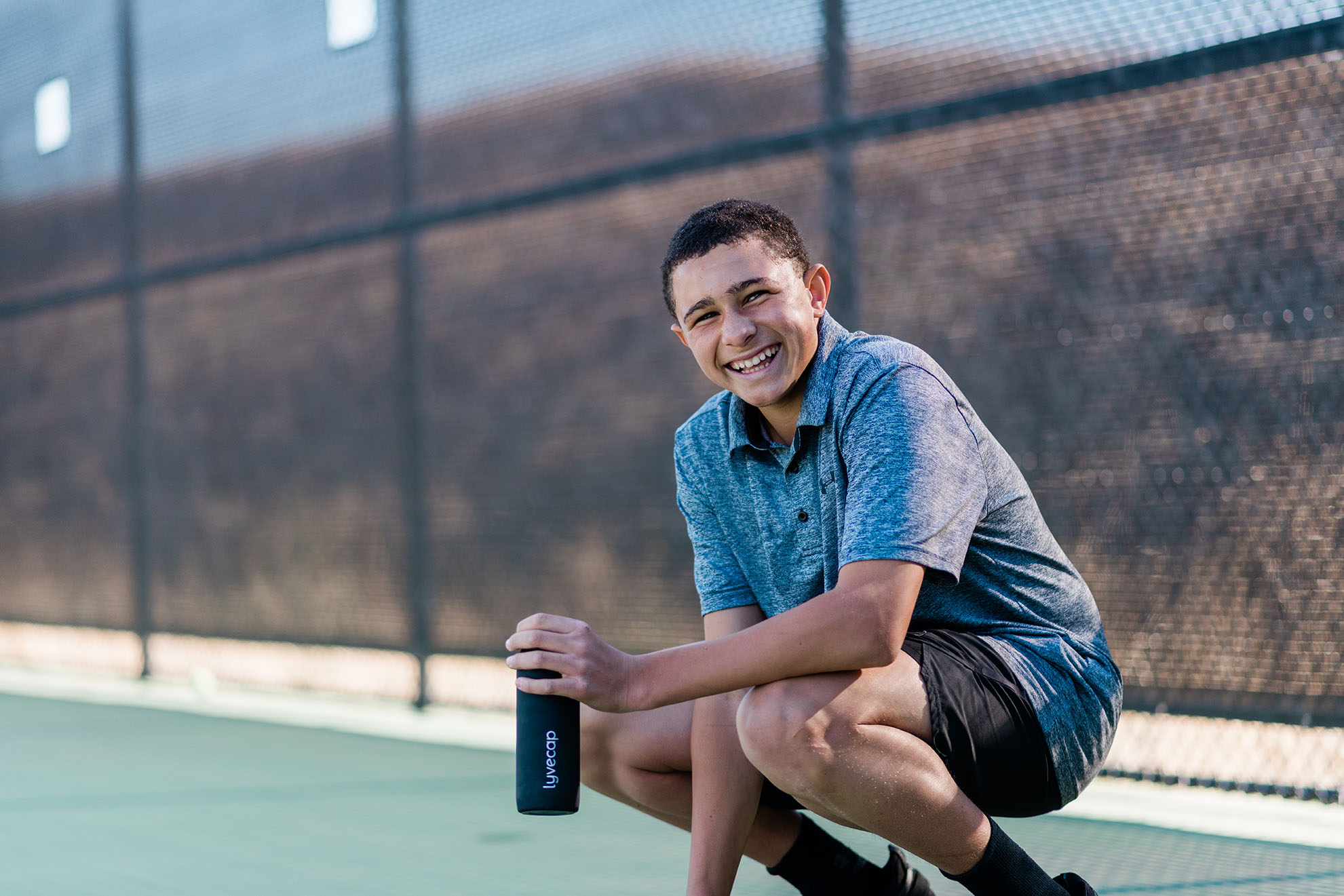 Junior Athlete Aston Davies is smiling on a tennis court with a Lyvecap bottle 