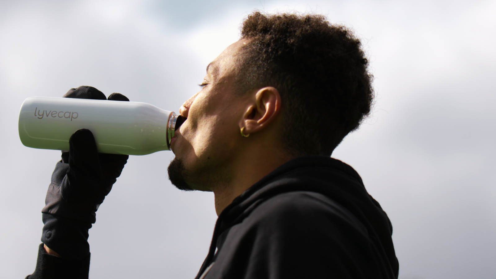 A photo of professional runner with the Brooks Beasts, Isaiah Harris, drinking out of a Lyvecap bottle. 